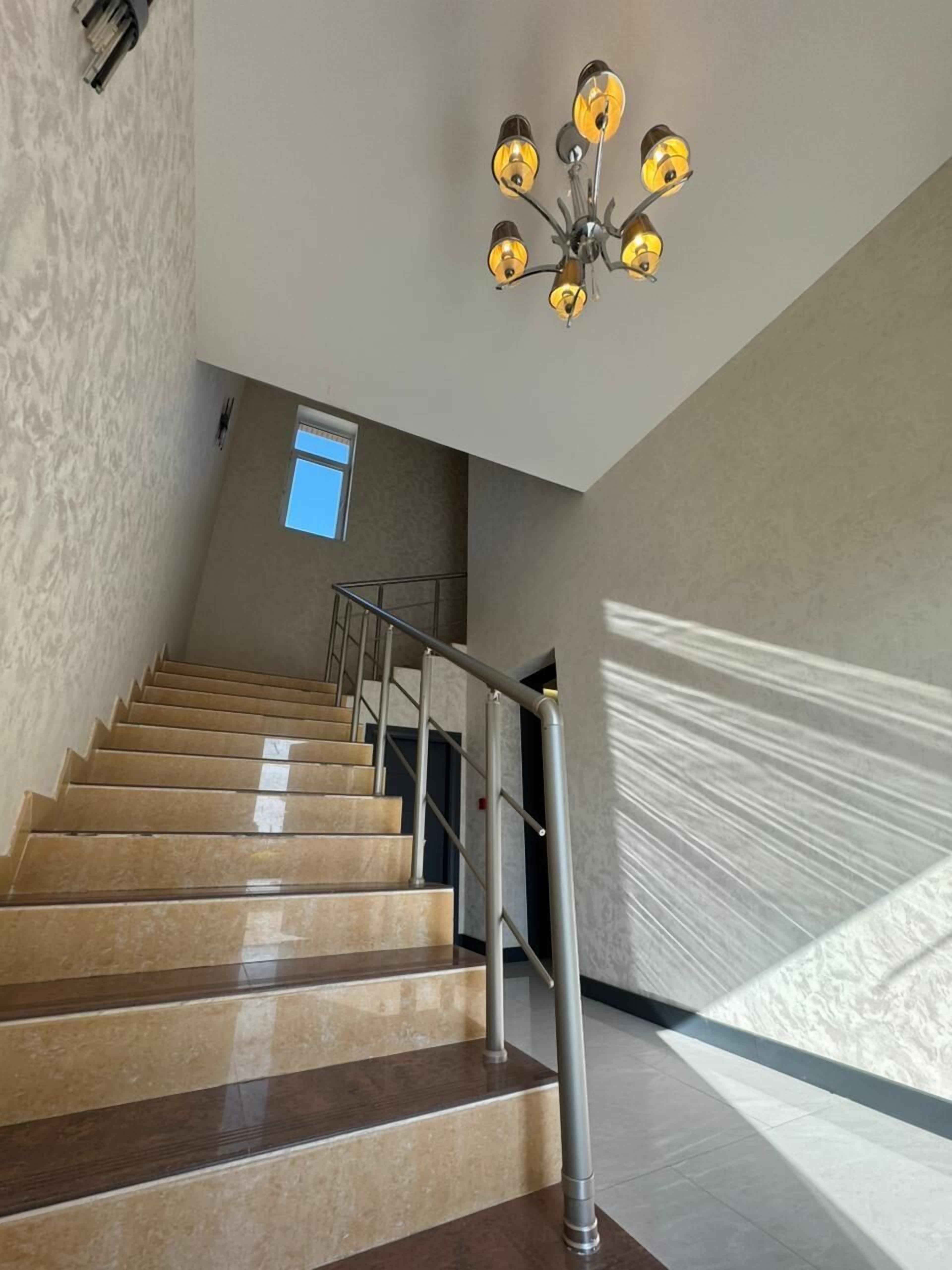A staircase with a metal railing, a chandelier, and a window.