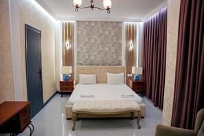 Una habitación de hotel con una cama grande, mesitas de noche, un banco y un armario.