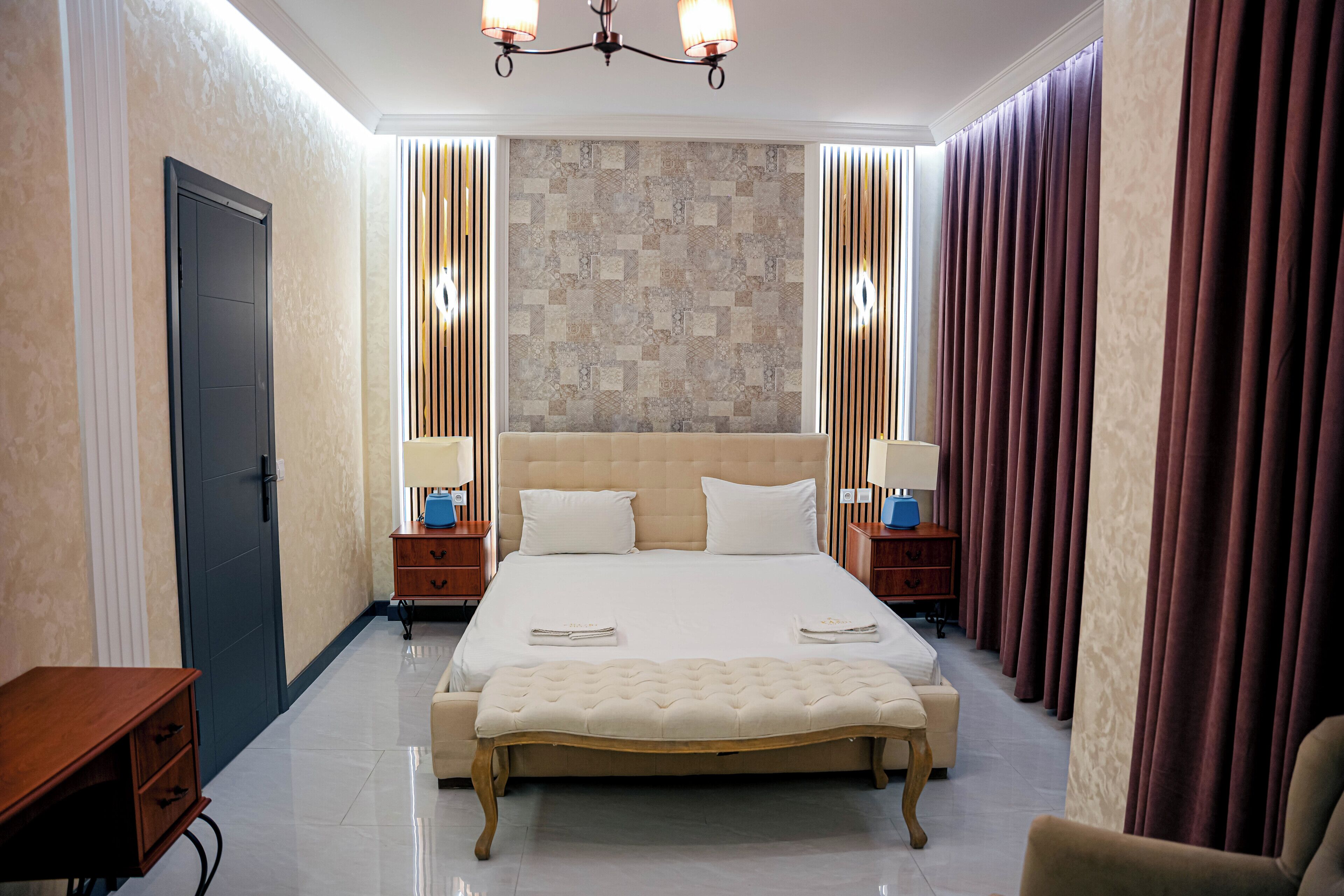 Una habitación de hotel con una cama grande, mesitas de noche, un banco y un armario.