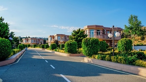 Een woonstraat met huizen, een heldere lucht en goed onderhouden groen.