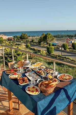A table set with various dishes, a teapot, and a view of the sea and greenery. - Khazri Resort & Villas (Baku)