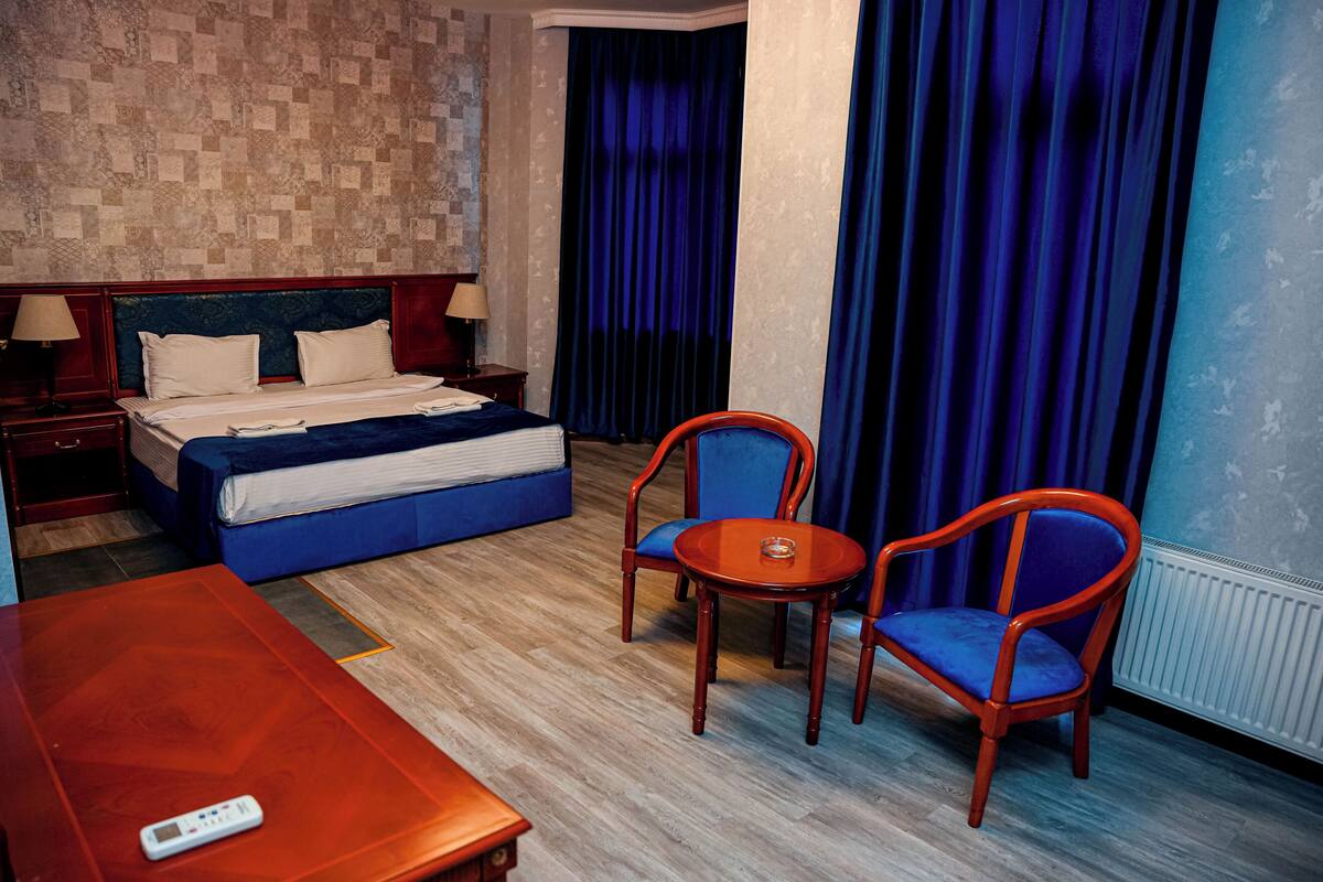 Habitación de hotel con una cama, dos sillas, una mesa y un control remoto.