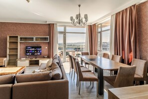 A modern hotel room with a dining area, a TV, and a view of the city. - Khazri Resort & Villas (Baku)