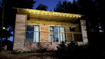 Un edificio rústico con fachada de ladrillo, amplias ventanas y una pérgola de madera con luces.