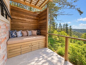 A wooden deck with a built-in bench, a brick wall, and a view of a forested landscape. - Myrtle Forest Retreat Cabin • Verandah + Braai (Plettenberg Bay)