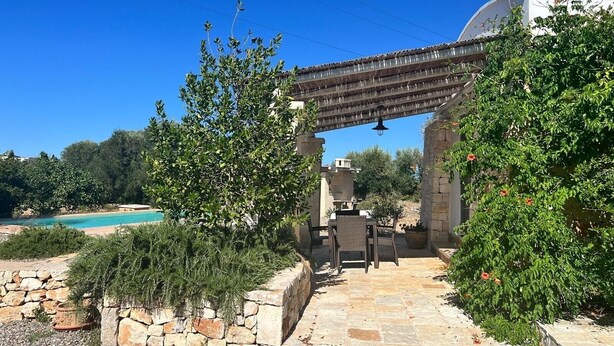 Uma trilha de pedra leva a um pátio com móveis de exterior, piscina e uma estrutura de pérgola.