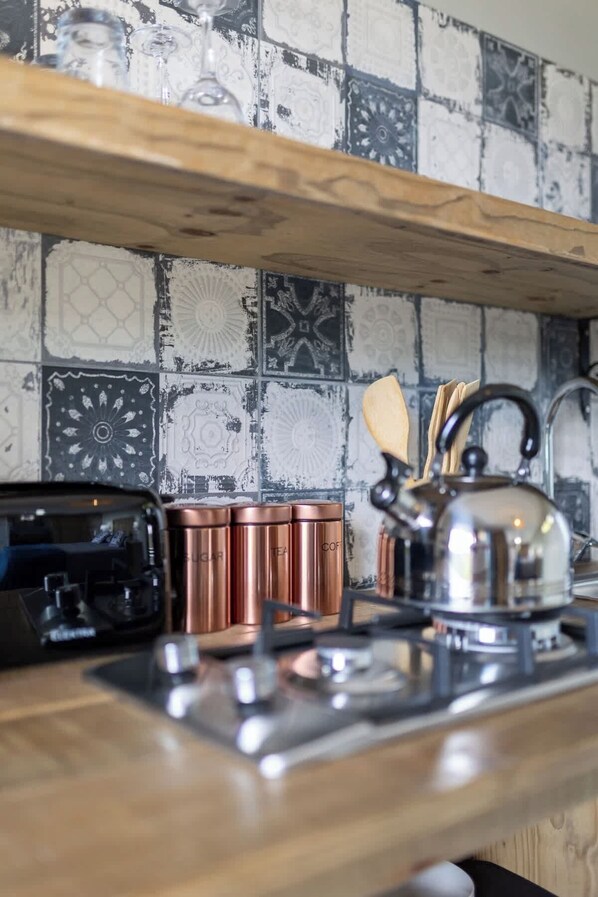 A kitchen with a patterned backsplash, a kettle, and stainless steel appliances. - Pine Forest Retreat Cabin • Verandah + Braai (Plettenberg Bay)