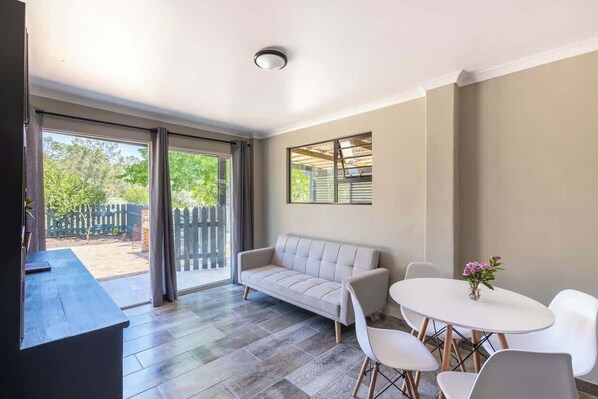 A room with a sofa, a table, and chairs, a window, and a door leading outside.