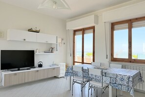 A modern kitchen with a flat-screen TV, white cabinetry, and a dining area with a patterned tablecloth. - P095 - Porto Recanati, new three-room apartment  (Porto Recanati)
