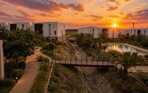 Ein modernes Resort mit mehreren Gebäuden, einem Swimmingpool und Blick auf einen Sonnenuntergang.