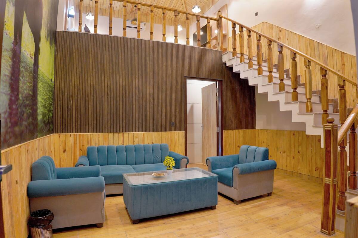 Amplia sala de estar con una escalera de madera, un conjunto de sofá azul y una mesa de centro con un jarrón.