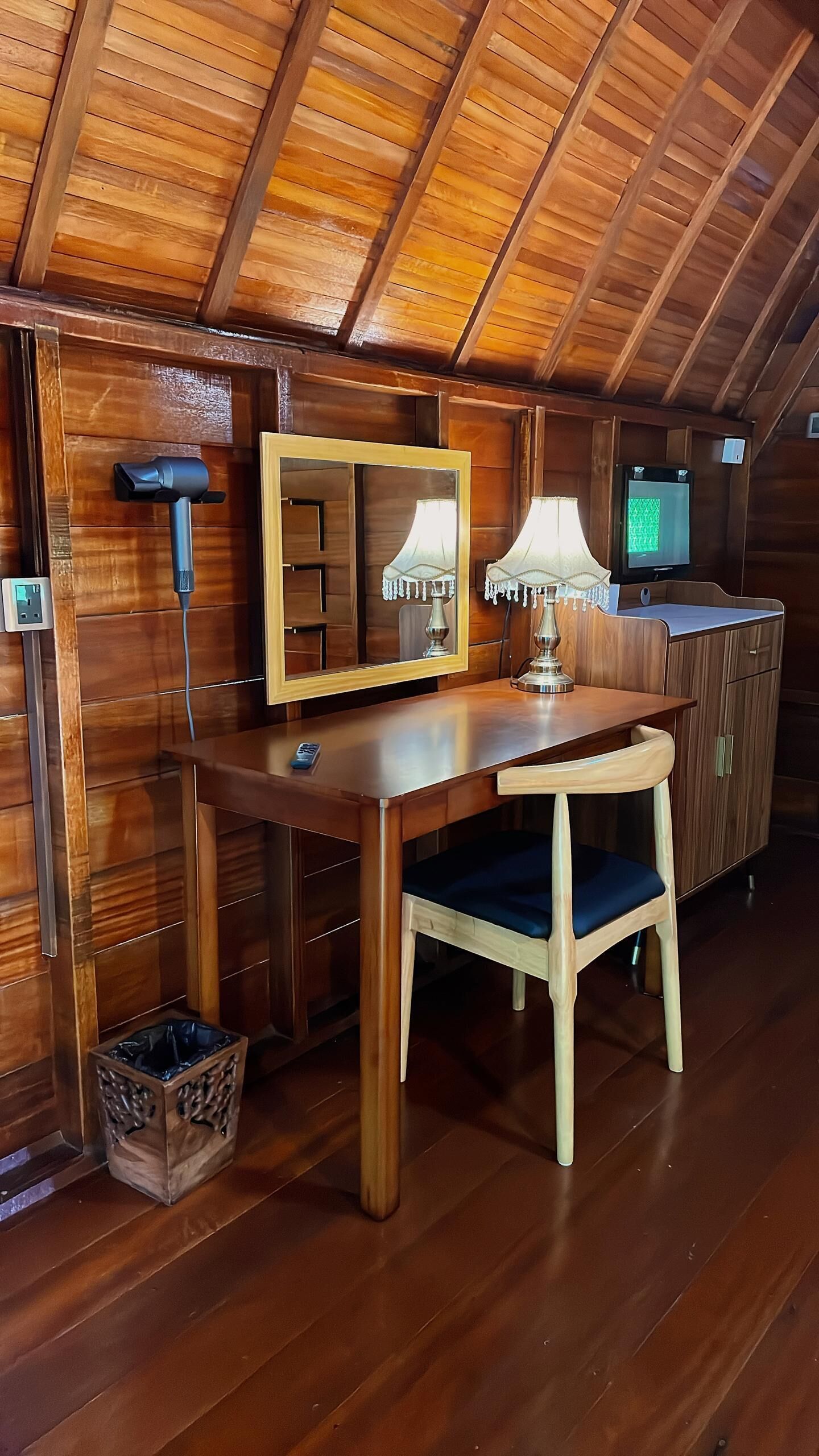 Un intérieur en bois comprenant un bureau, une chaise, une lampe, un miroir, un téléviseur et une poubelle.