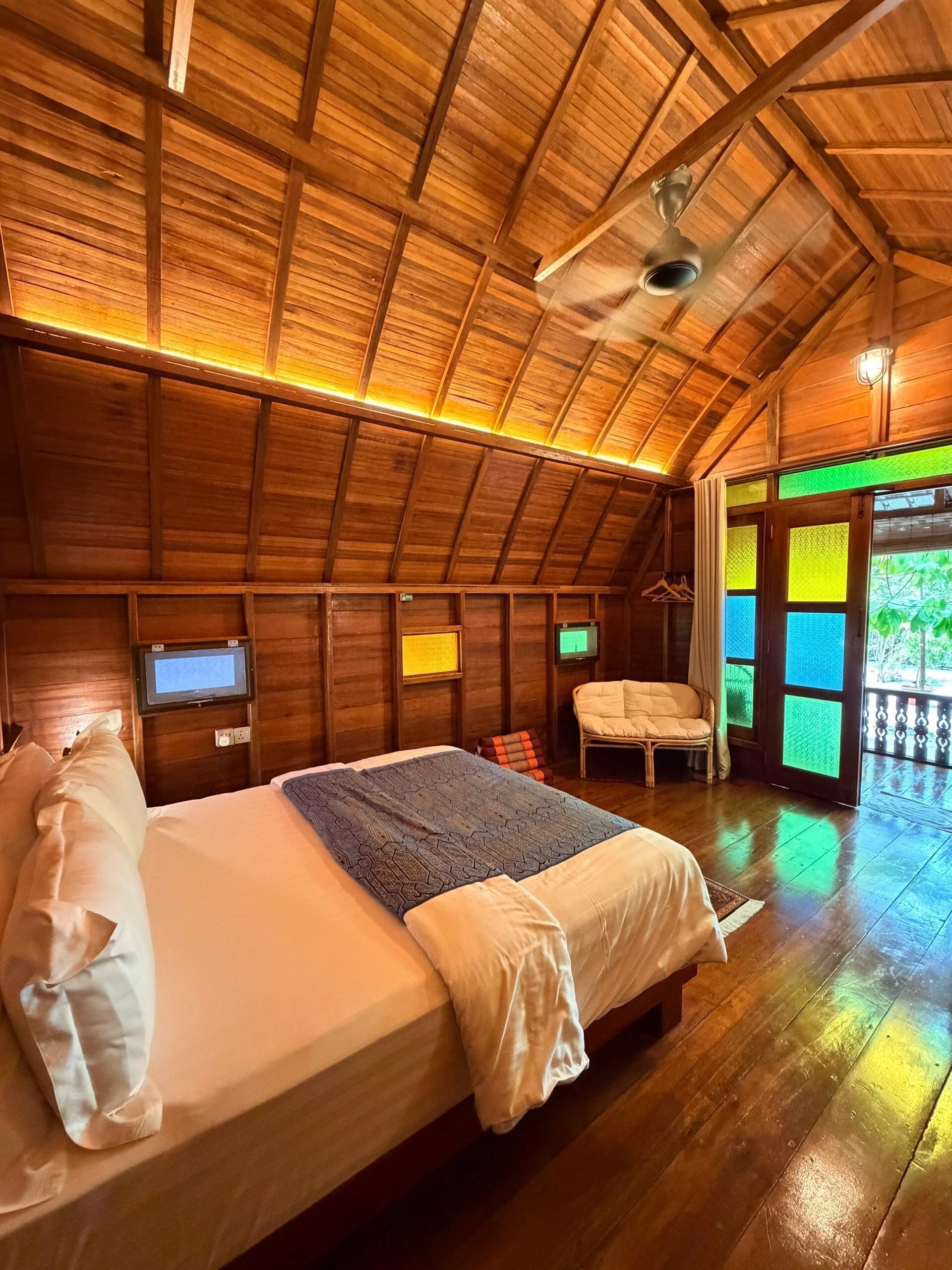 Una habitación de madera con cama, una silla, un televisor y un ventilador de techo.
