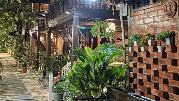 A traditional wooden building with a balcony, potted plants, and a brick wall. - Golden Chenang Village (Langkawi)