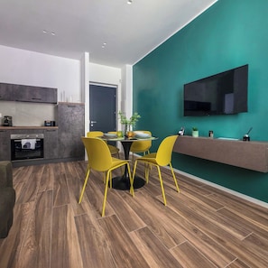 A modern kitchen with built-in appliances, a dining area with yellow chairs, and a teal accent wall.