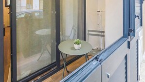 A balcony with a table and chair, a potted plant, and a view of a building through a glass door. - Grigio Perla Suites  (Manfredonia)