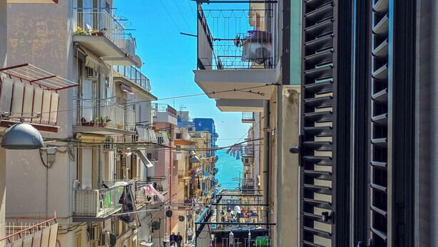 A narrow urban street with multi-story buildings, balconies, and parked cars. - Grigio Perla Suites  (Manfredonia)