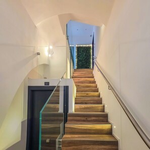 A modern staircase with glass railings and wooden steps, leading to a room with a green wall and a window.
