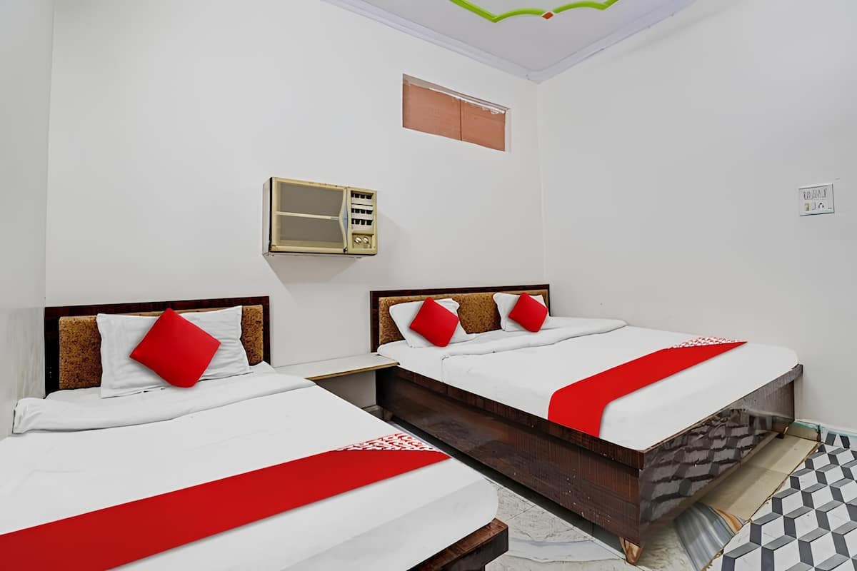 Ein Hotelzimmer mit zwei Betten, einem kleinen Fenster, einer Wand-Klimaanlage und einem Fliesenboden.