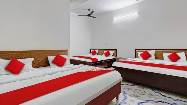 A hotel room with three beds, each with a red and white bedspread and matching pillows.