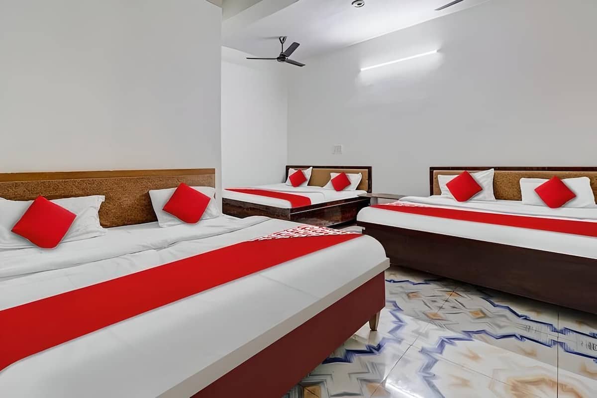 Ein Hotelzimmer mit drei Betten, jeweils mit einer roten und weißen Bettdecke sowie passenden Kissen.