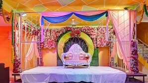 A stage with a white ornate sofa, floral decorations, and draped fabric.
