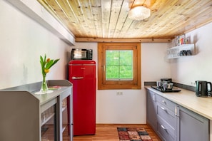 A compact kitchen with a red refrigerator, a microwave, a window, and a wooden ceiling.