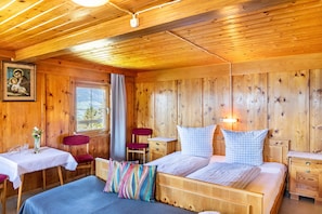 A wooden cabin room with a bed, bedside tables, a desk with a chair, and a window.
