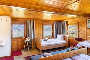 Une chambre dans un chalet en bois, comprenant un lit, un bureau, une chaise, une table et une fenêtre donnant sur la montagne.