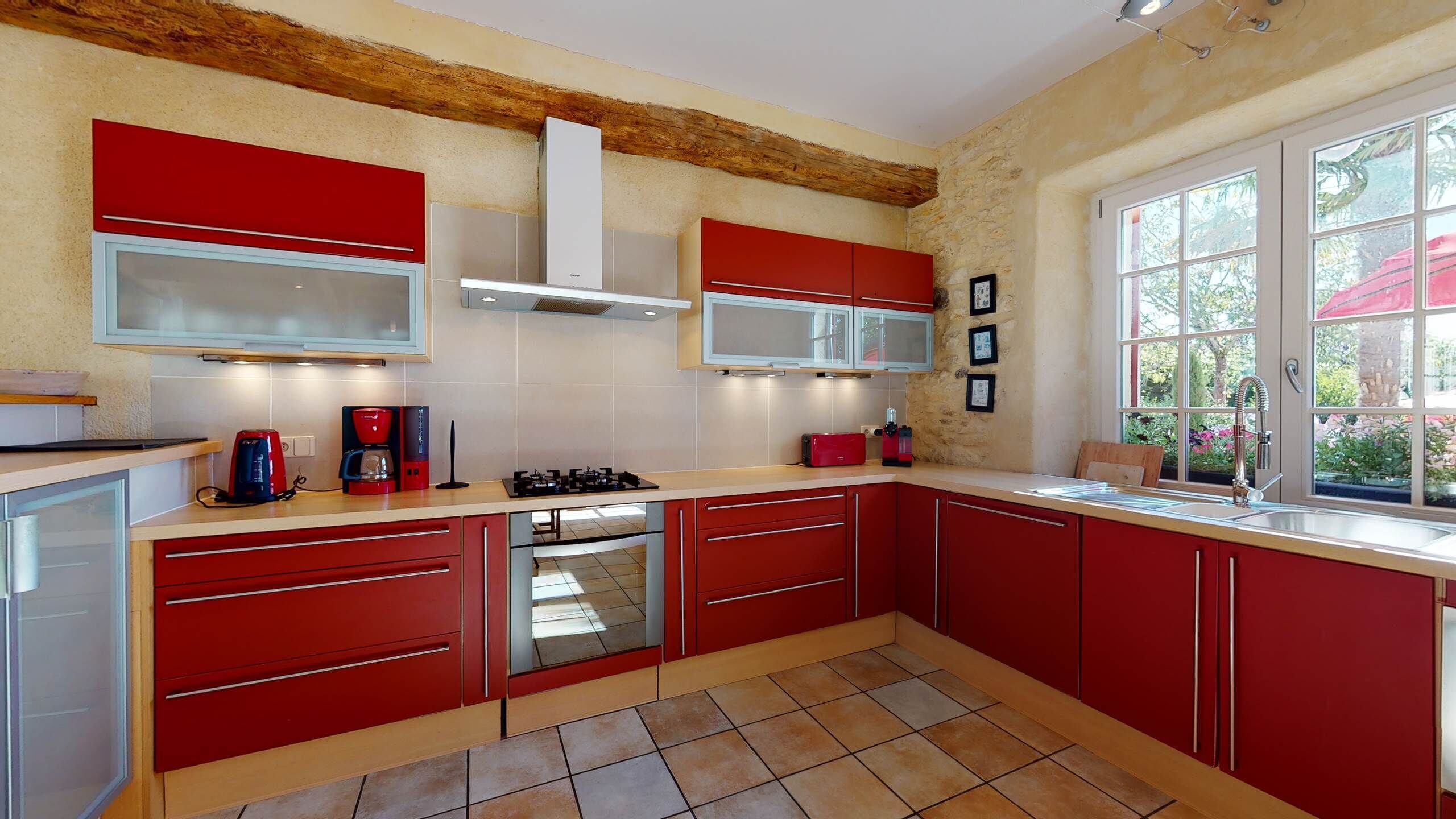 Una cocina con armarios rojos, estufa a gas, microondas y un ventanal con vistas a zonas verdes.