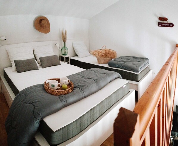 Une chambre avec deux lits, une tête de lit en bois, une table de chevet avec un vase et un panneau accroché au mur.