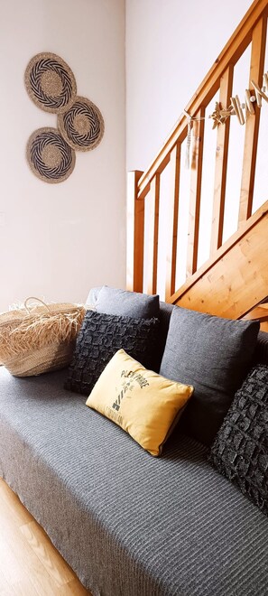 Un canapé gris avec trois coussins, un panier en osier et un escalier en bois.