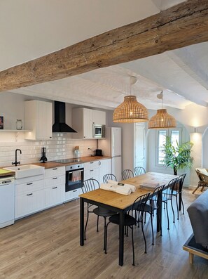 A modern kitchen with white cabinets, a wooden dining table, and hanging pendant lights.