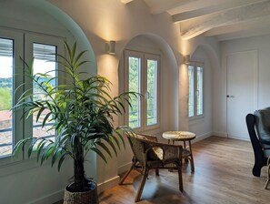 Ein Zimmer mit großen Fenstern, einem Blumentopf, Korbmöbeln und Holzboden.
