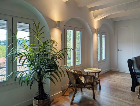A room with large windows, a potted plant, wicker furniture, and a wooden floor.