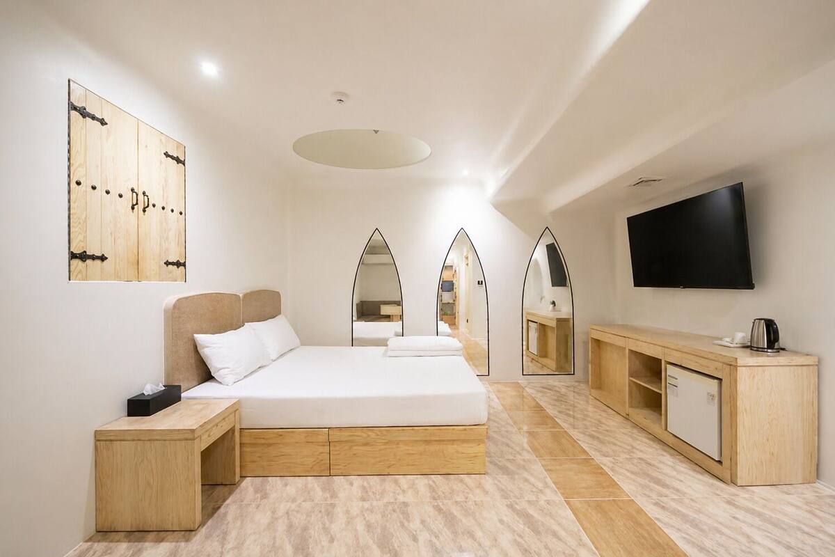 Une chambre d’hôtel moderne avec un grand lit, des meubles en bois, une télévision et plusieurs miroirs.