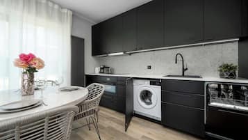 Una cocina moderna con armarios oscuros, lavadora integrada y una zona de comedor con sillas de mimbre.