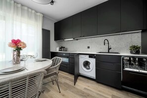 A modern kitchen with dark cabinets, a built-in washing machine, and a dining area with wicker chairs. - Spacious Apartment | Garden and Workspace (Wrocław)
