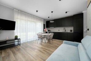 Una cocina moderna con armarios oscuros, un comedor con mesa y sillas redondas, un sofá azul claro y un televisor de pantalla plana montado en la pared.