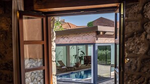 Ein Zimmer mit Steinwänden und einem Fenster mit Blick auf einen Swimmingpool sowie ein Backsteinhaus.