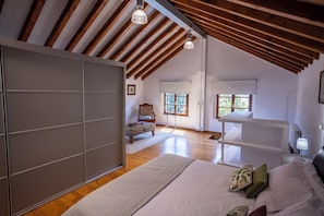 Een slaapkamer met een groot bed, houten balken, een raam en een stoel.