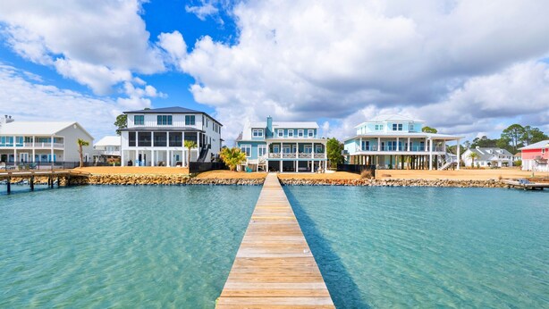 Una propiedad frente al agua con un muelle de madera que conduce a una casa de varios niveles y balcones.