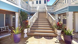 Un edificio de varios niveles con una escalera central, plantas en macetas y un banco de metal.