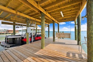 A wooden deck with a boat docked, a swing chair, and a view of the water. - Coastal Cottage Retreat | Pool, Boat Dock, & Minutes to Pirates Cove (Elberta)