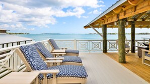 Una terraza de madera con sillones de descanso y un espacio techado con vistas al mar.
