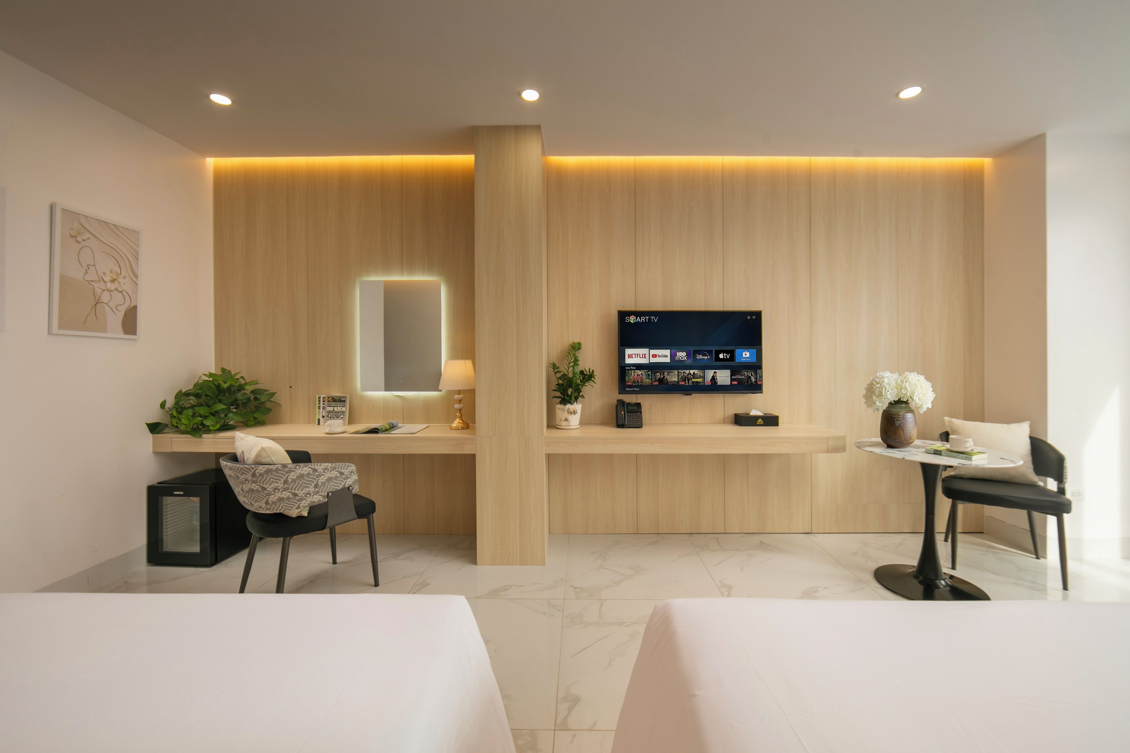 A hotel reception area with a flat-screen TV displaying streaming services, a reception desk, a waiting area with a chair and a small table, and a reception counter with a plant.