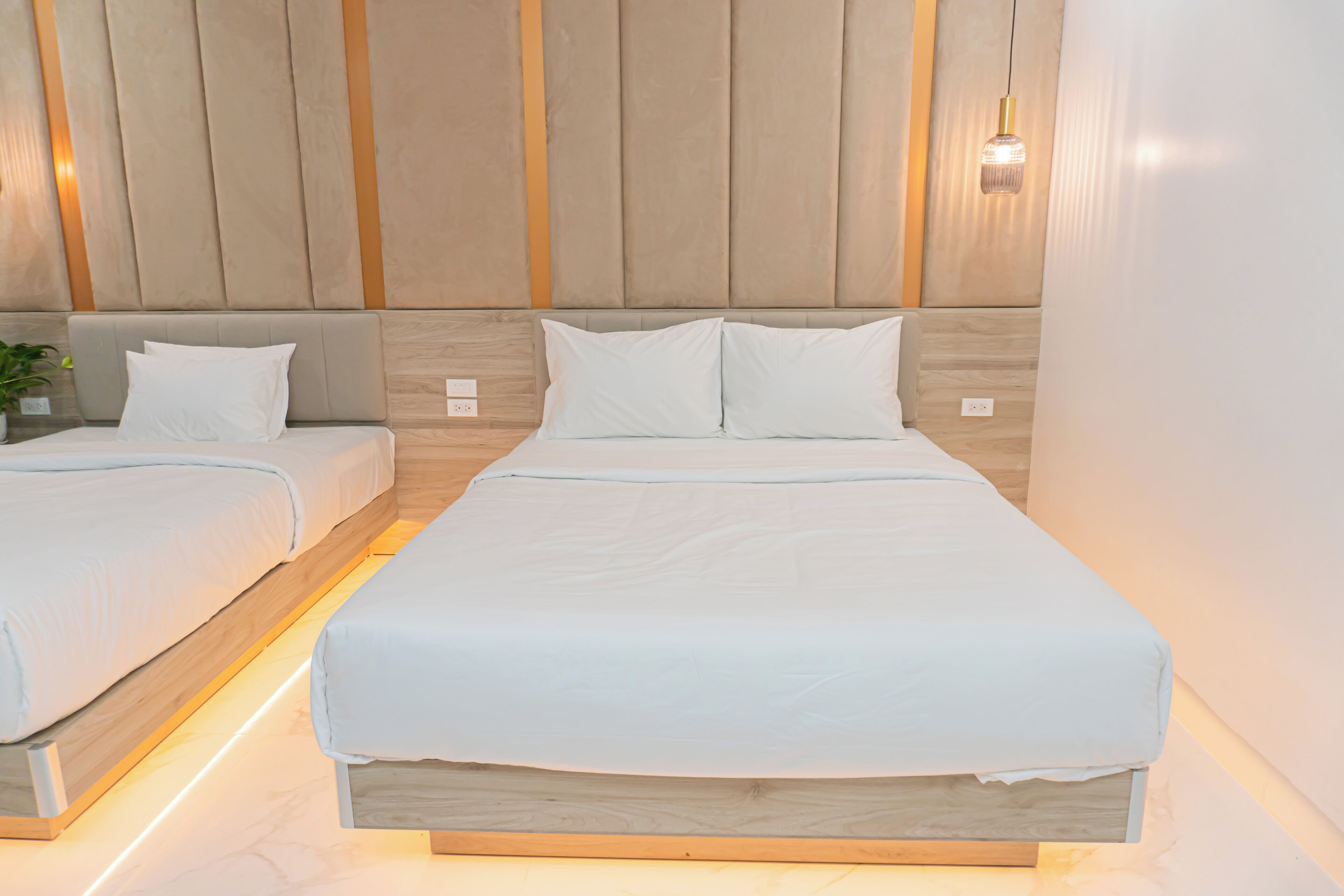 Een hotelkamer met twee bedden, houten hoofdeinden en een wandlamp.
