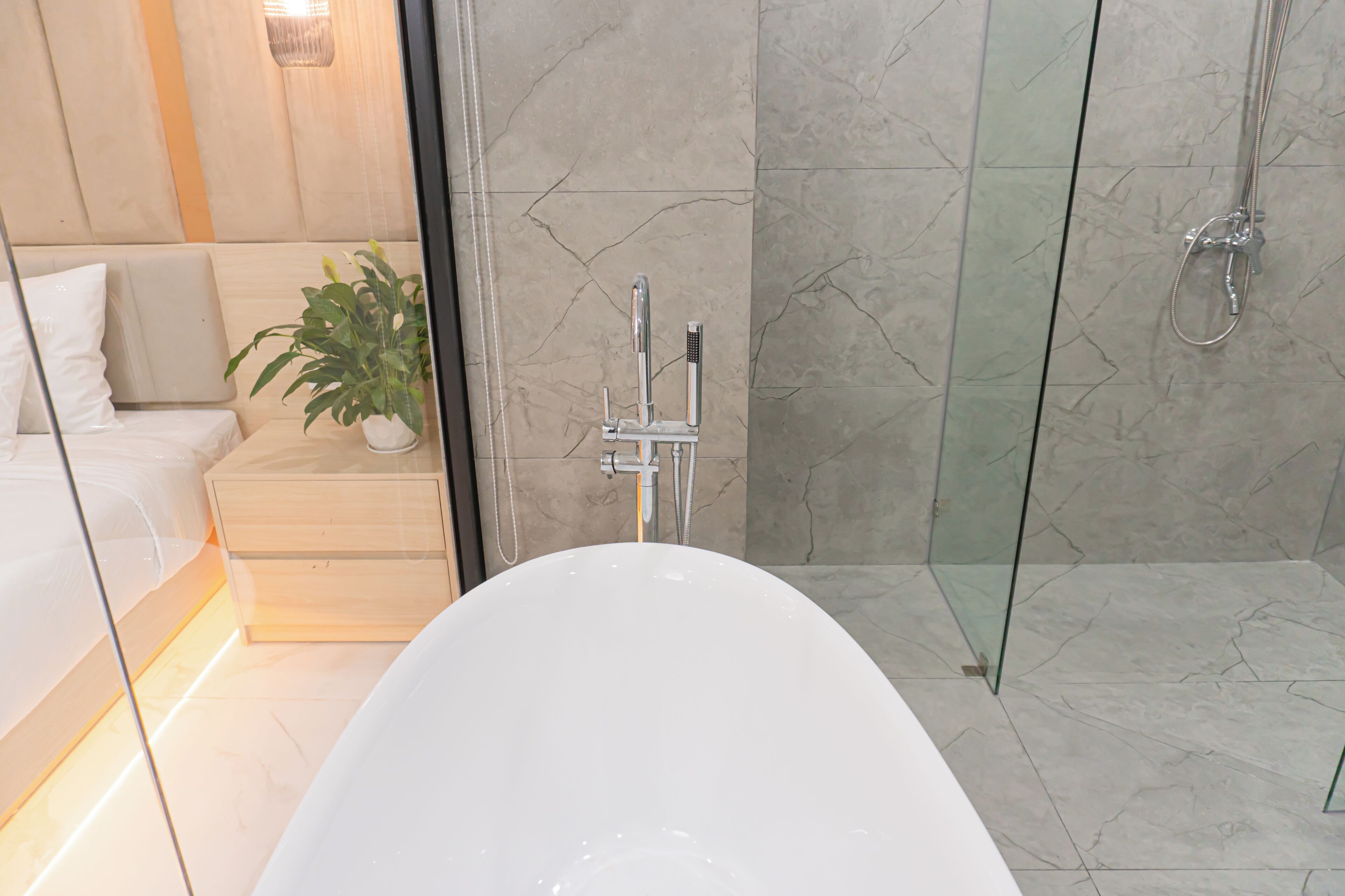 A modern bathroom with a freestanding bathtub, a glass shower enclosure, and a potted plant.