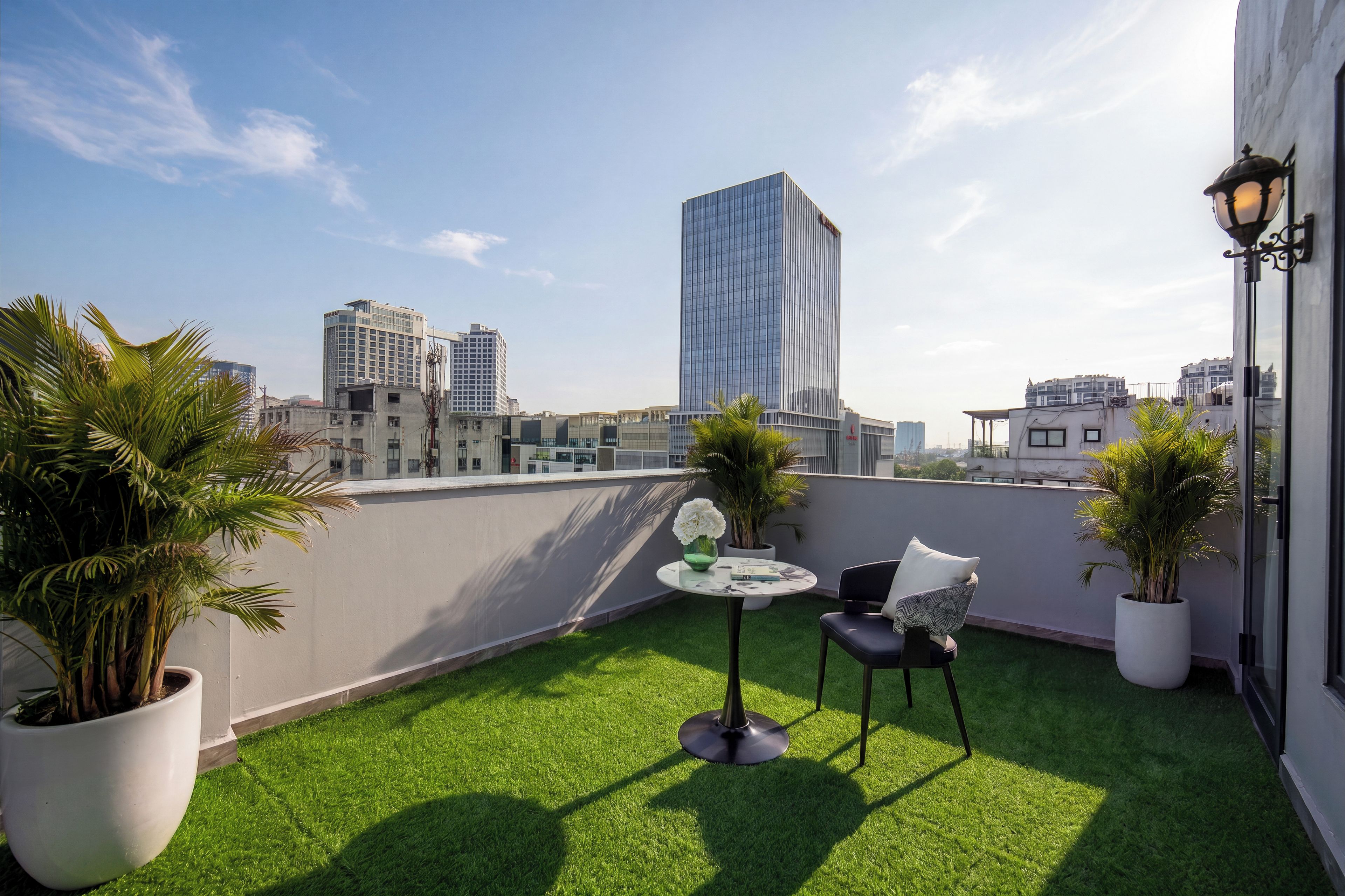 Eine Dachterrasse mit Kunstgrasanlage, zwei Stühlen, einem kleinen Tisch und Topfpflanzen.