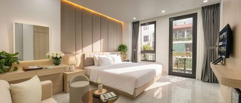 A modern hotel room with a bed, sofa, bedside tables, a TV, and a balcony with curtains.